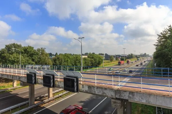 Fiets- en voetgangersbrug De Wel over de snelweg A2 bij Vught, met verkeer en zonnig weer op de achtergrond.